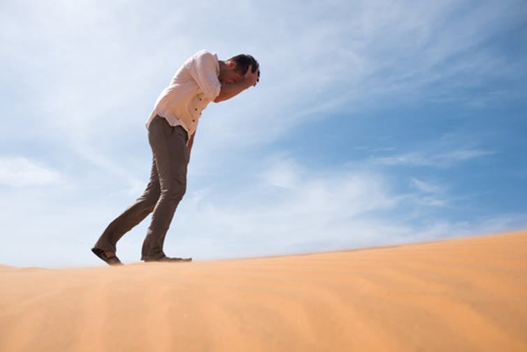 man walking in the desert clutching his head