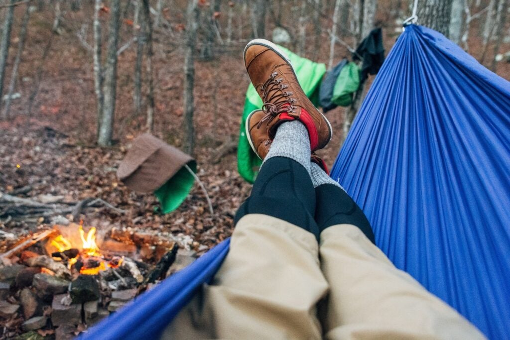 person camping in hammock near a campfire in the woods