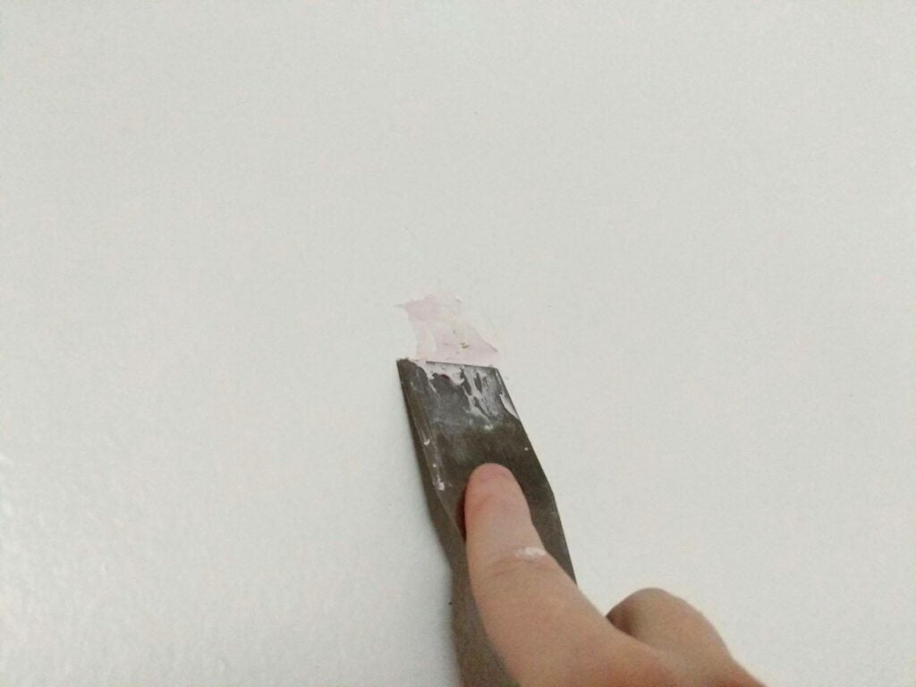 a person smearing putty over a hole in drywall with a putty knife