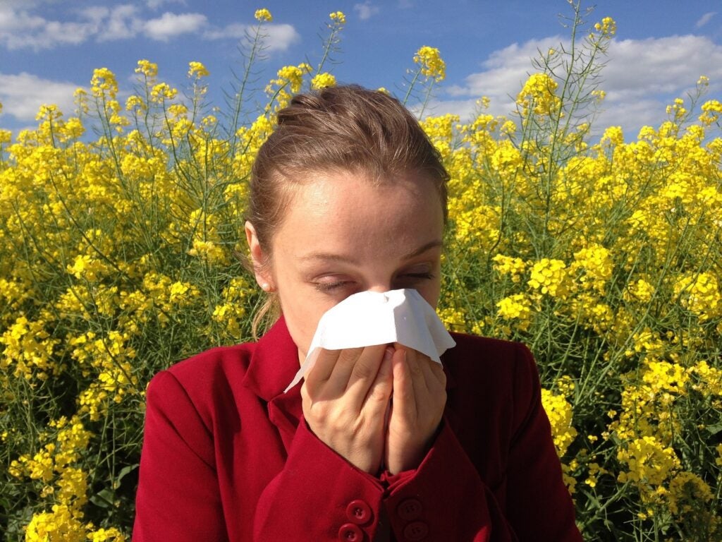 a woman blowing her nose into a tissue in front of a field of flowers