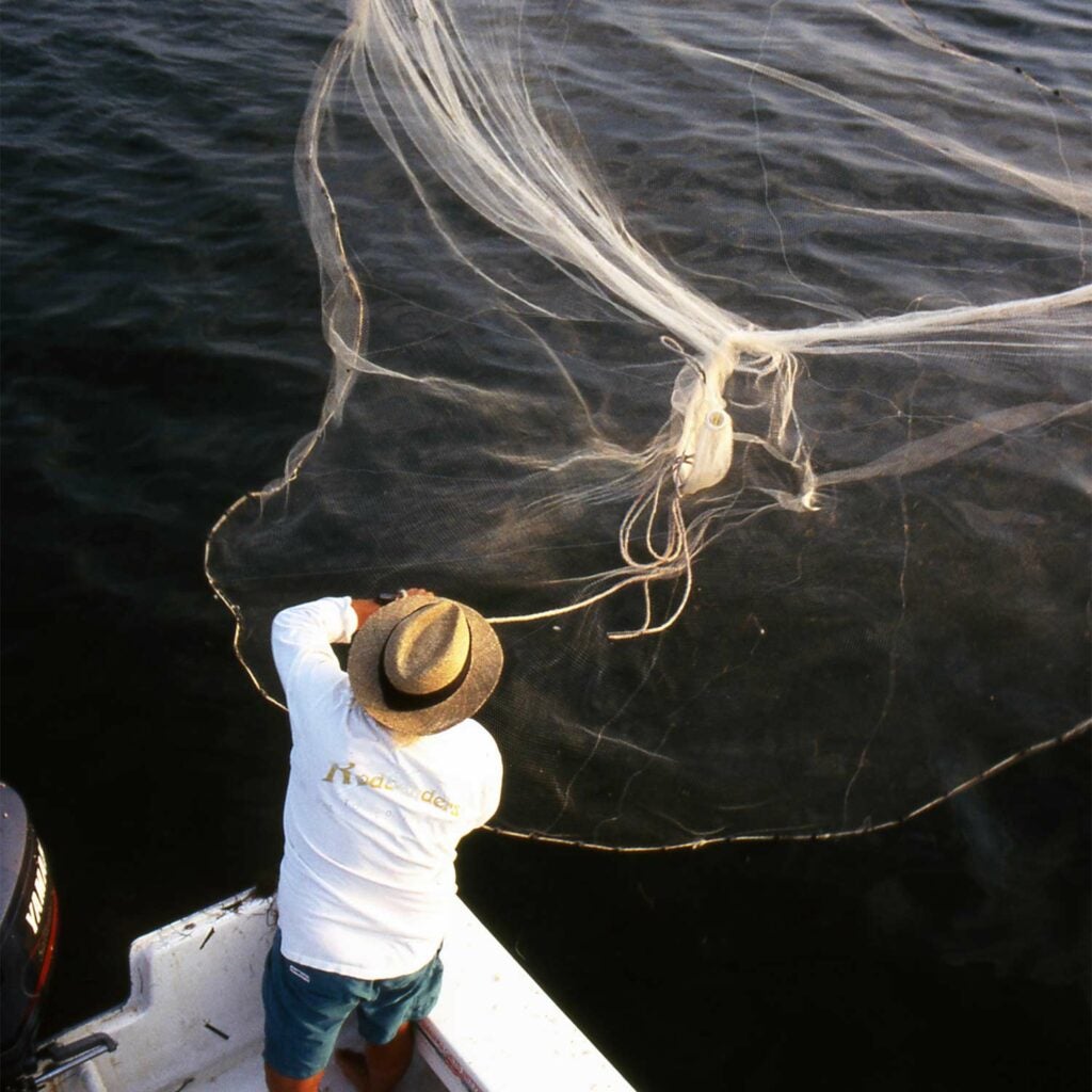 fisherman throwing a cast net into the ocean