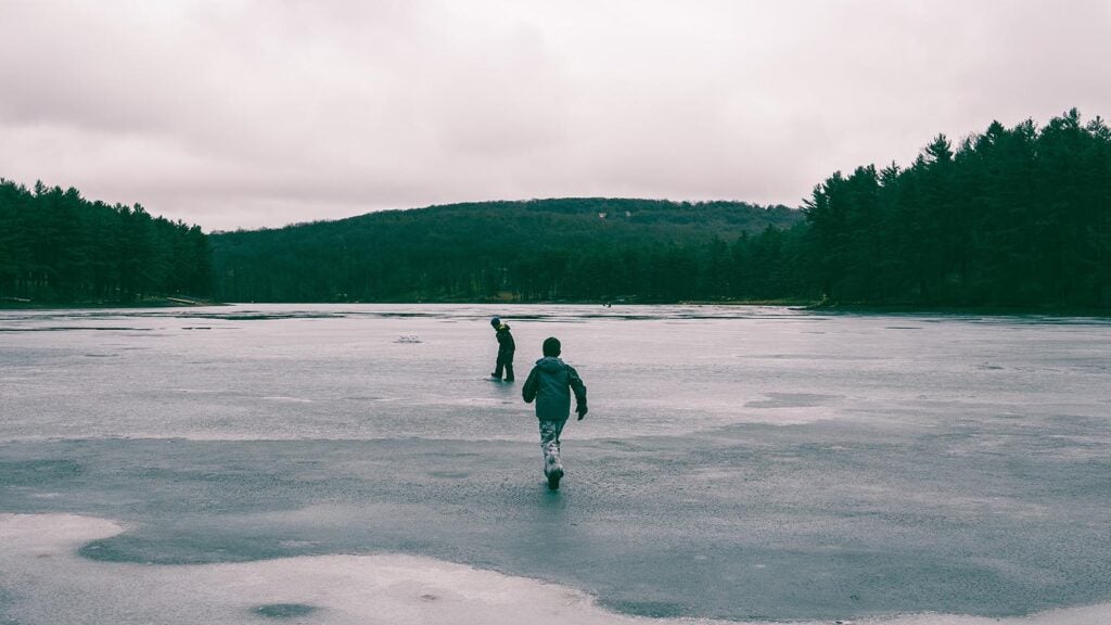 Two kids running into a frozen lake