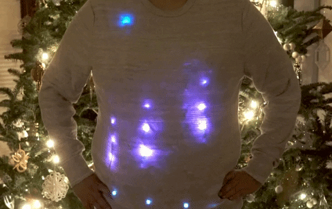 a person wearing an Arduino-powered LED sweater in front of a Christmas tree
