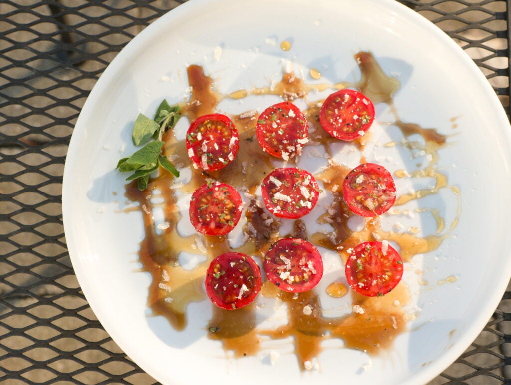 halved cherry tomatoes on a plate with parmesan cheese, marjoram, olive oil, balsamic vinegar, and other spices