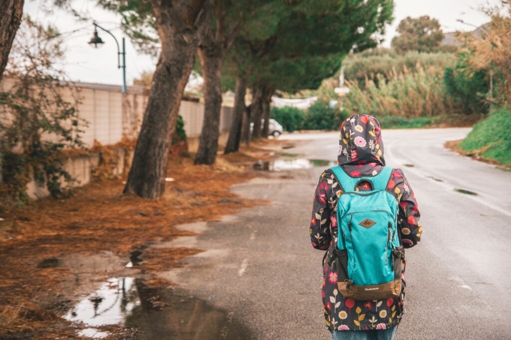 a person in a rain jacket walking on a wet road while wearing a teal backpack