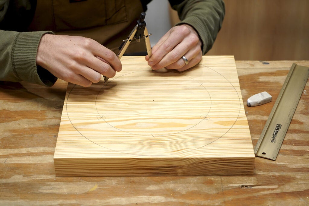 a person using a compass and a pencil to draw circles on pine wood to make the seat of a three-legged stool