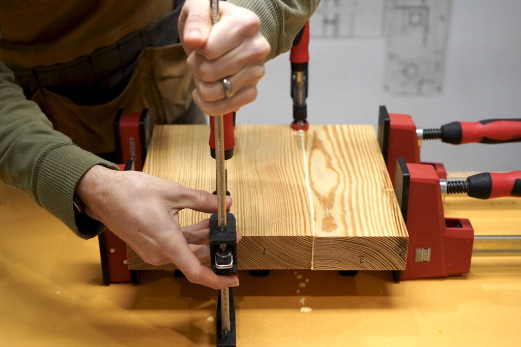 a person clamping pine wood together with glue to form the seat of a three-legged stool