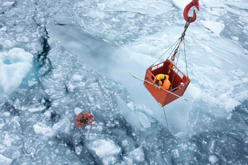 person in crane basket with rope attached to measuring instruments in icy water
