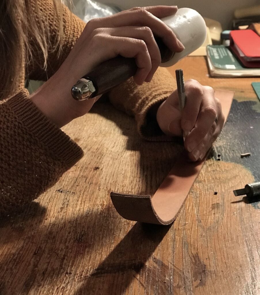 a leatherworker using a maul and a metal stamping tool on a piece of leather