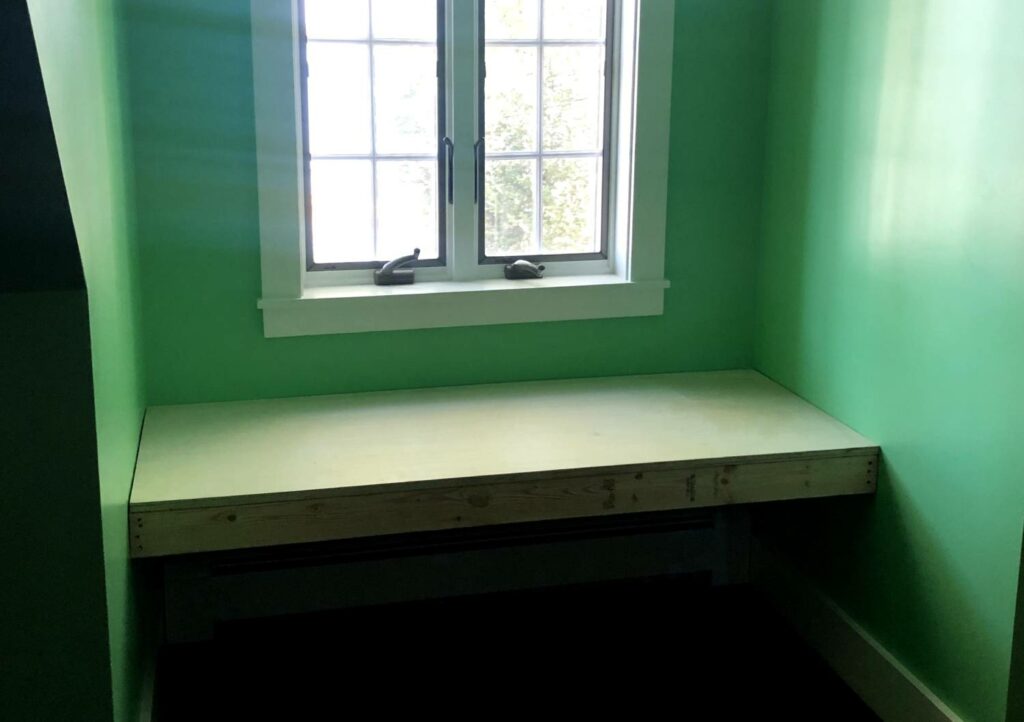 a window seat base made out of two-by-fours and topped with plywood, in a dormer window