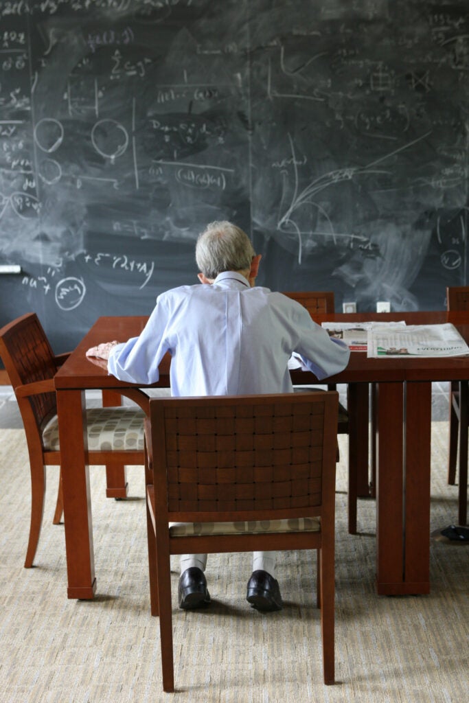 A man working at a table in front of a blackboard covered in equations.