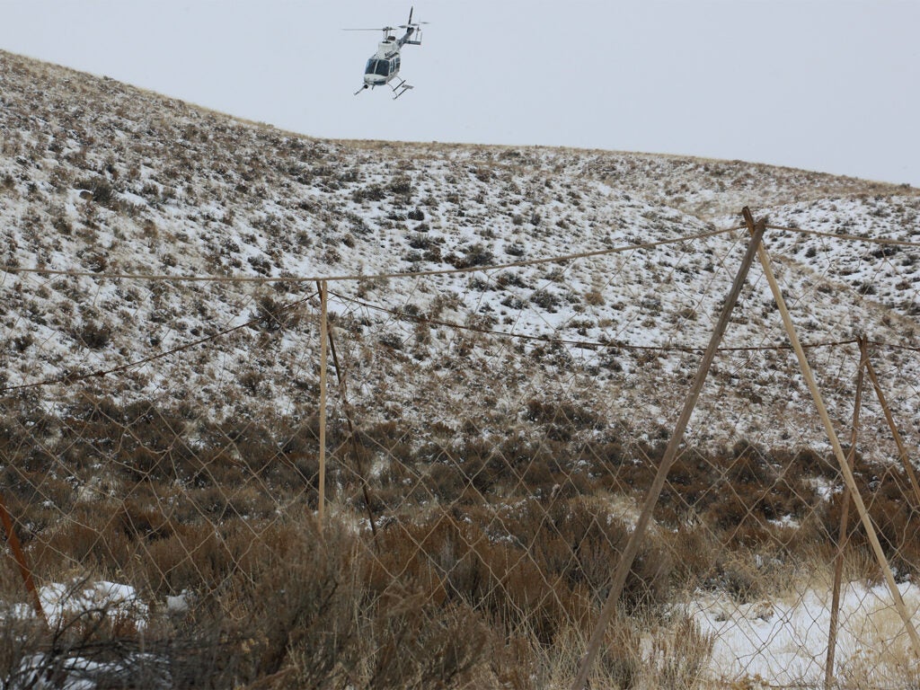 A helicopter flying over a hillside covered in snow.