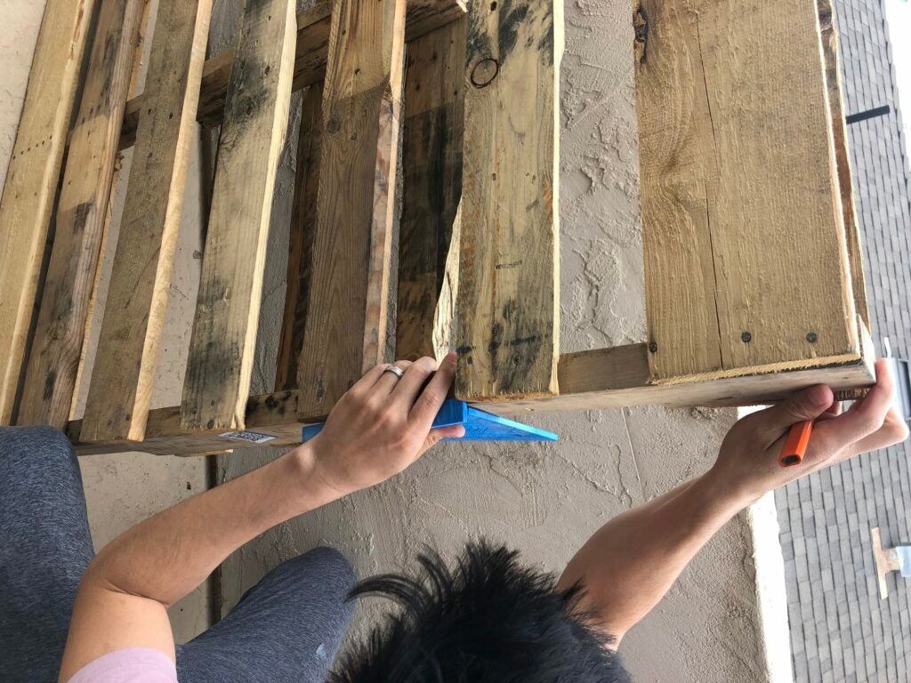 a person marking where they want to cut on a wooden pallet that will eventually become a wall-mounted wine rack