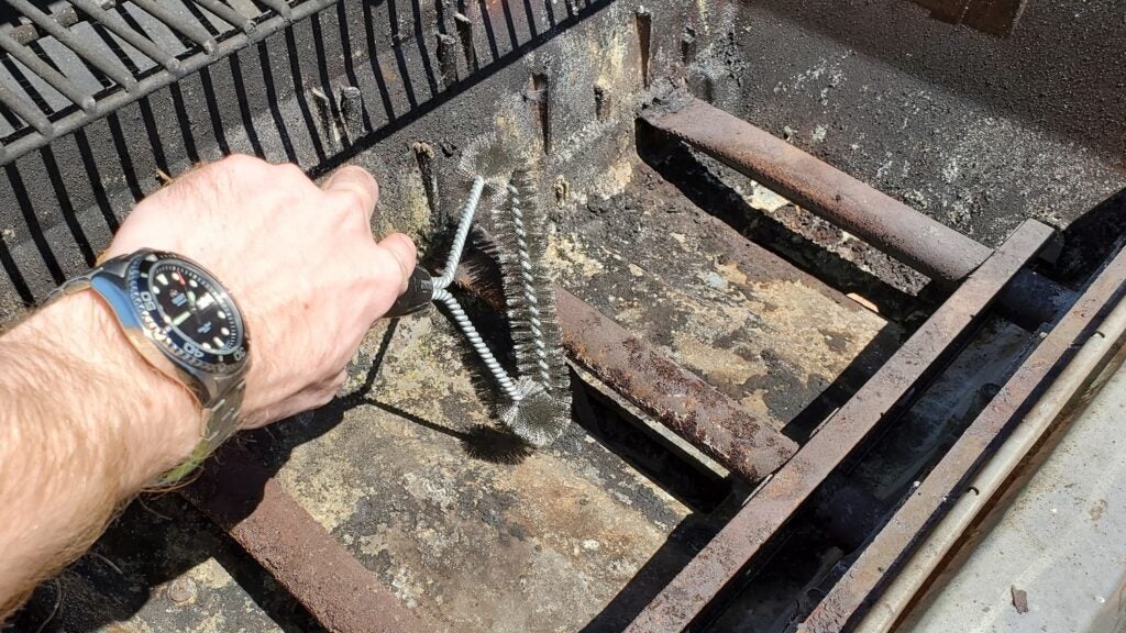 a person brushing a gas grill burner with a wire grill brush