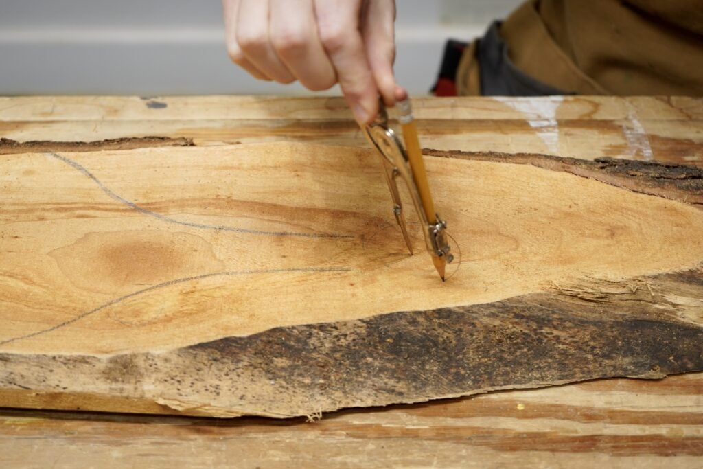 a person using a compass and a pencil to make a homemade cutting board out of a piece of live edge cherry