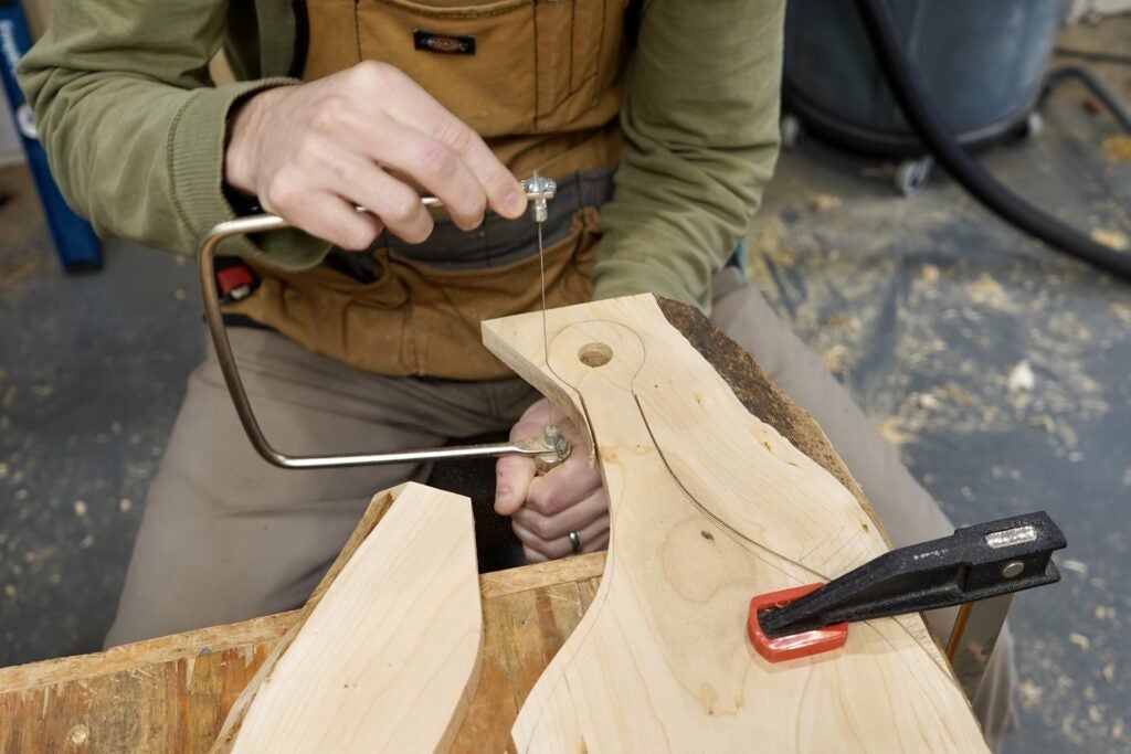 a person using a coping saw to cut the tight curves of a cutting board handle