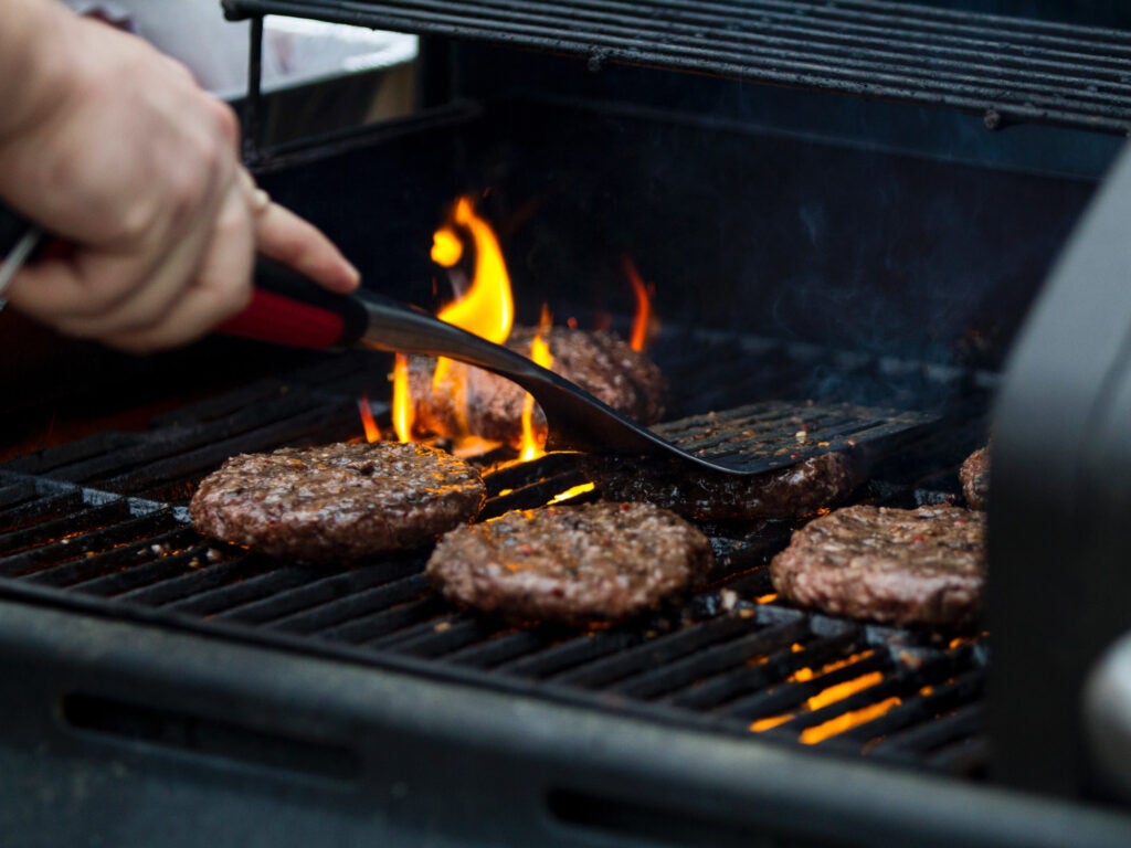 a person cooking burgers on a grill.