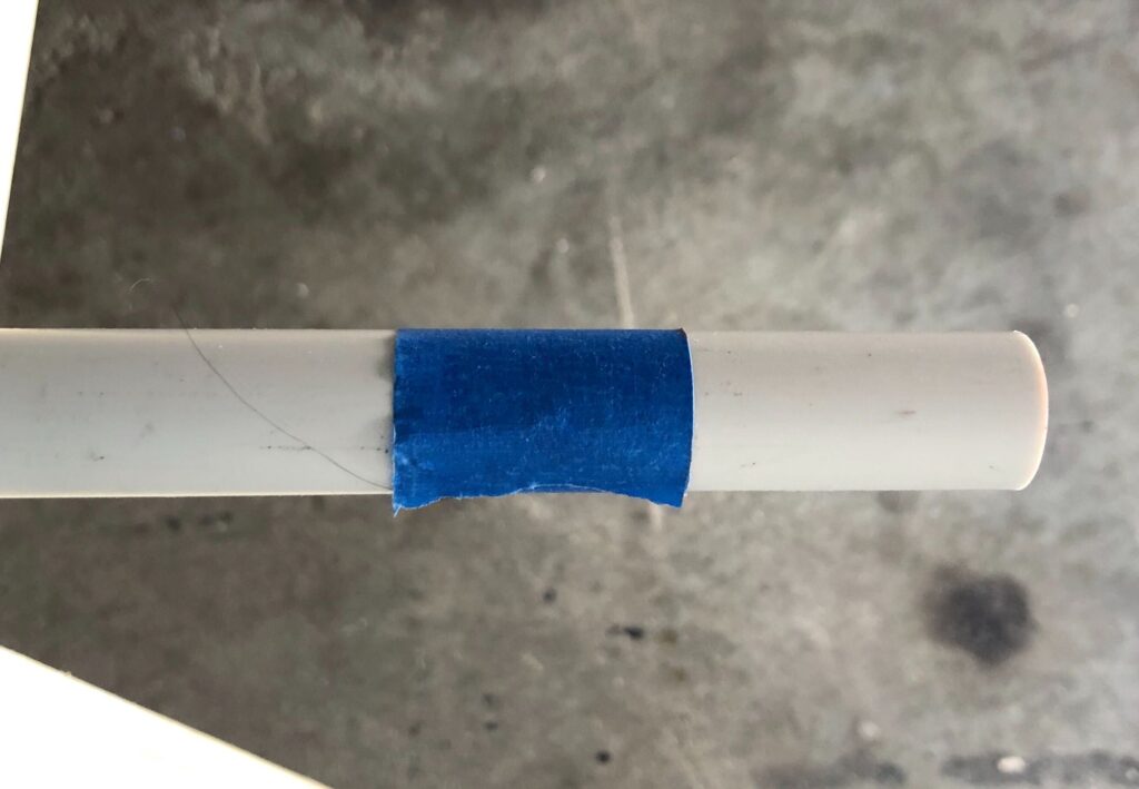 a piece of blue masking tape wrapped around a plastic PVC pipe