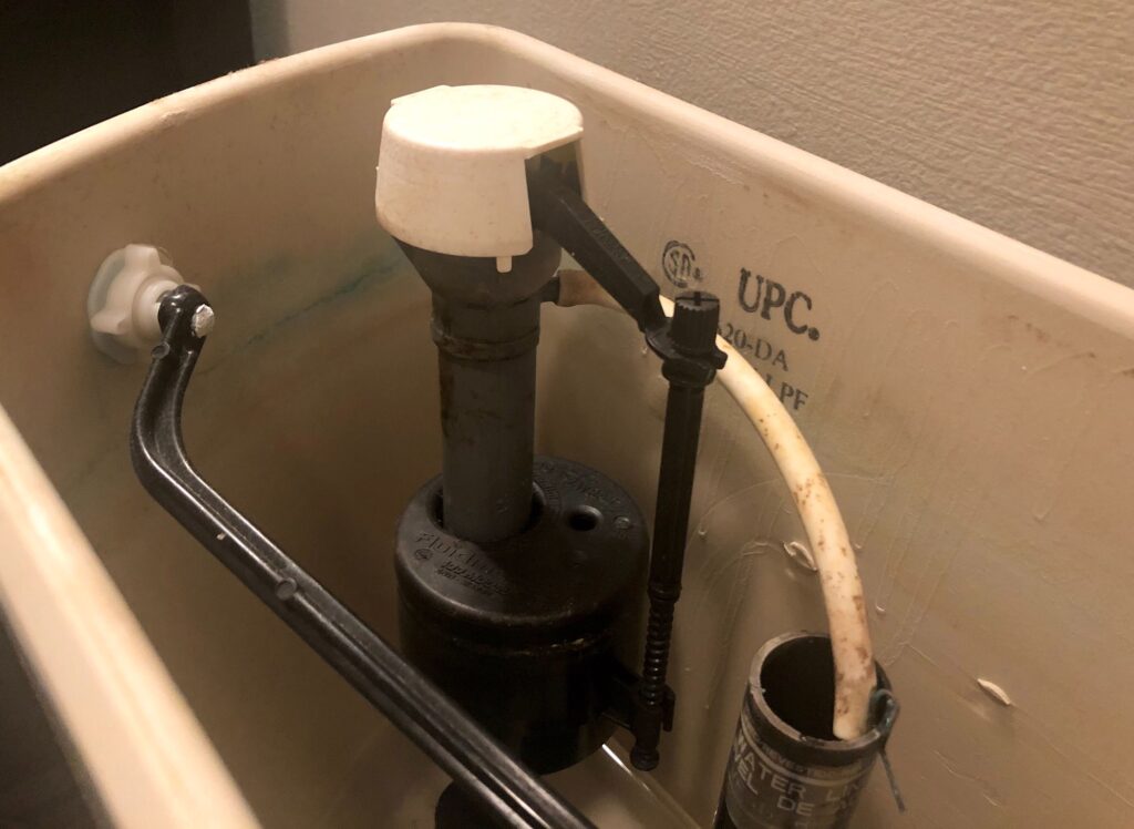 the inside of a toilet tank, showing the flush lever, or trip lever, the fill valve with integral float, or float valve, the refill tube, and the overflow tube