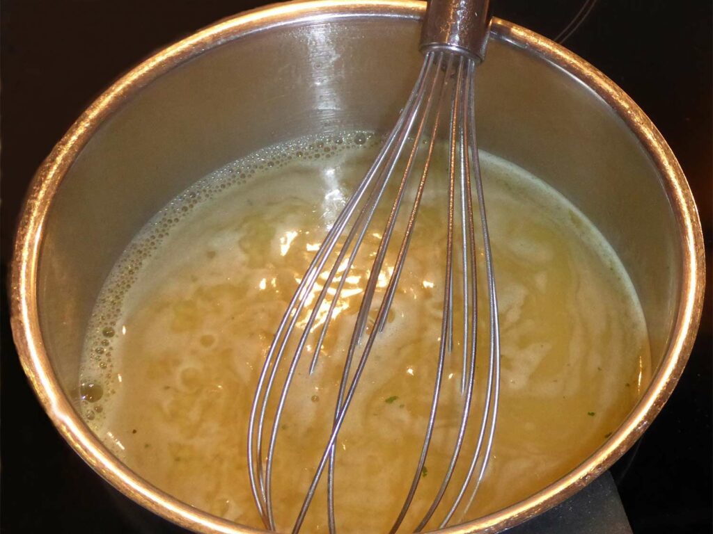 A metal whisk in a large pot of boiling bone broth