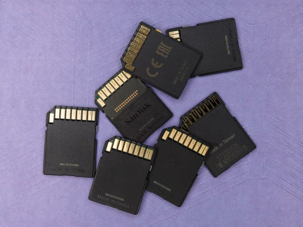 Seven SD cards in a loose pile on a purple surface.