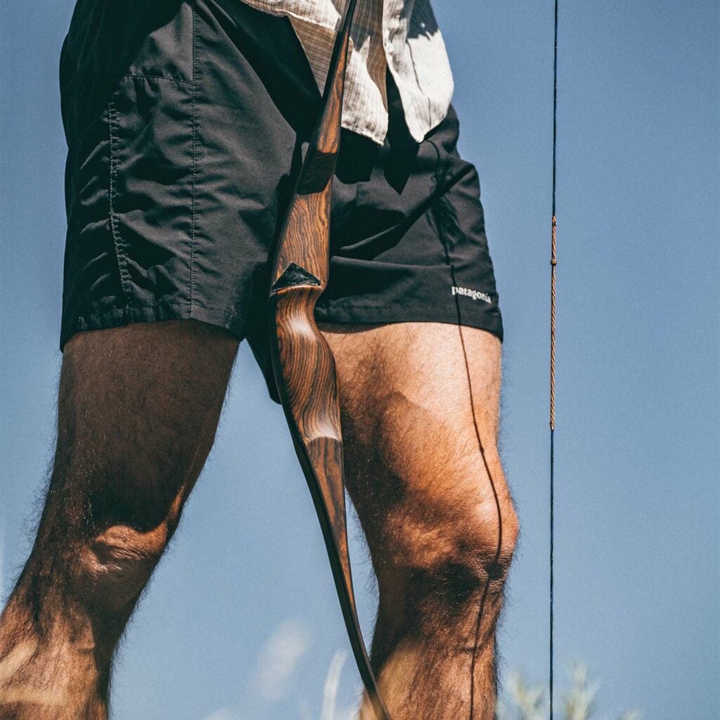 A hunter in shorts holds a traditional bow during a stalk and run hunt.