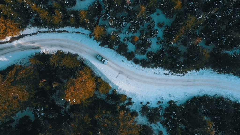 Birds-eye view of a car on a snowy road, flanked by trees.