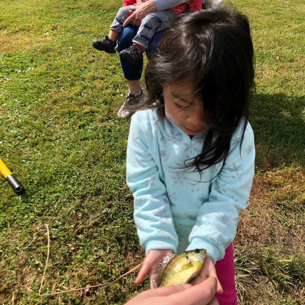 A young girl holds a small fish in her hands.