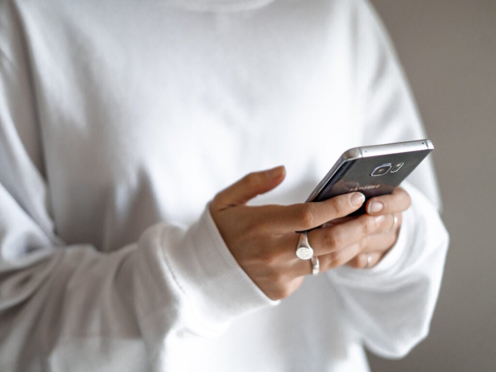 A person in a white sweatshirt holding a phone in their hands.